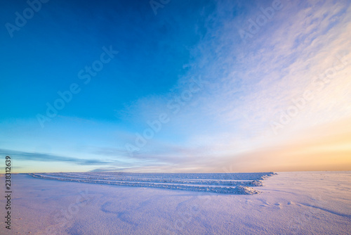 tire tracks on snow-covered field with winter sky during amazing sunrise 