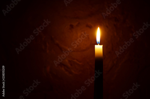 One yellow tall candle flame burning on dark red blurred background with copy space for text. Advent or memorial prayer candle flame.