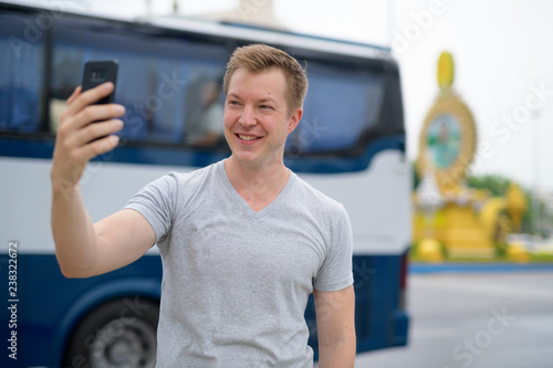 Young happy tourist man taking selfie against Ratchadamnoen street in Bangkok photo