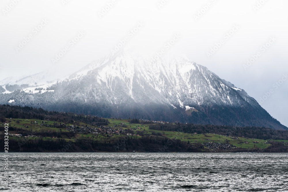 Close-up of Niesen mountain snow peak in clouds shot from other side of Lake Thun over Spitz area in Switzerland
