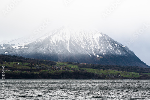 Close-up of Niesen mountain snow peak in clouds shot from other side of Lake Thun over Spitz area in Switzerland