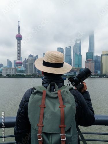Photography Vertical image of a man traveler with holding camera is looking at View of Shanghai city skyline in the morning