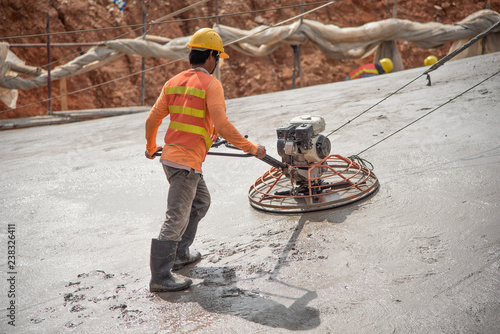 Construction worker wear standard safety uniform pouring and leveling fresh concrete at construction site