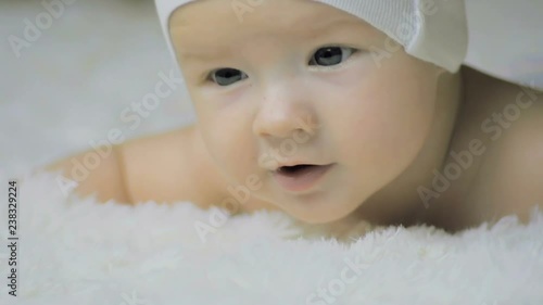 Close-up of a six-month baby in a headdress lying on a white blanket on the crib.