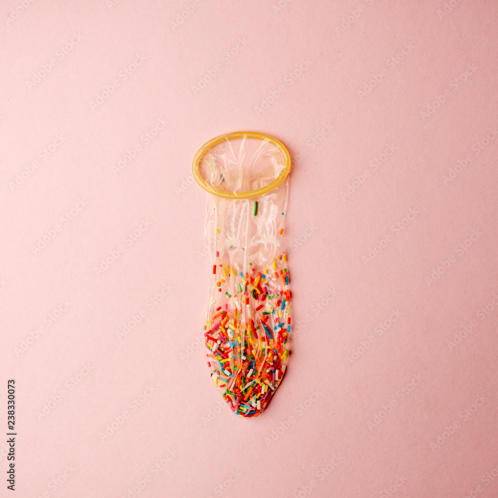a condom full of nonpareils of many colors on pink background, love saint valentine concept
