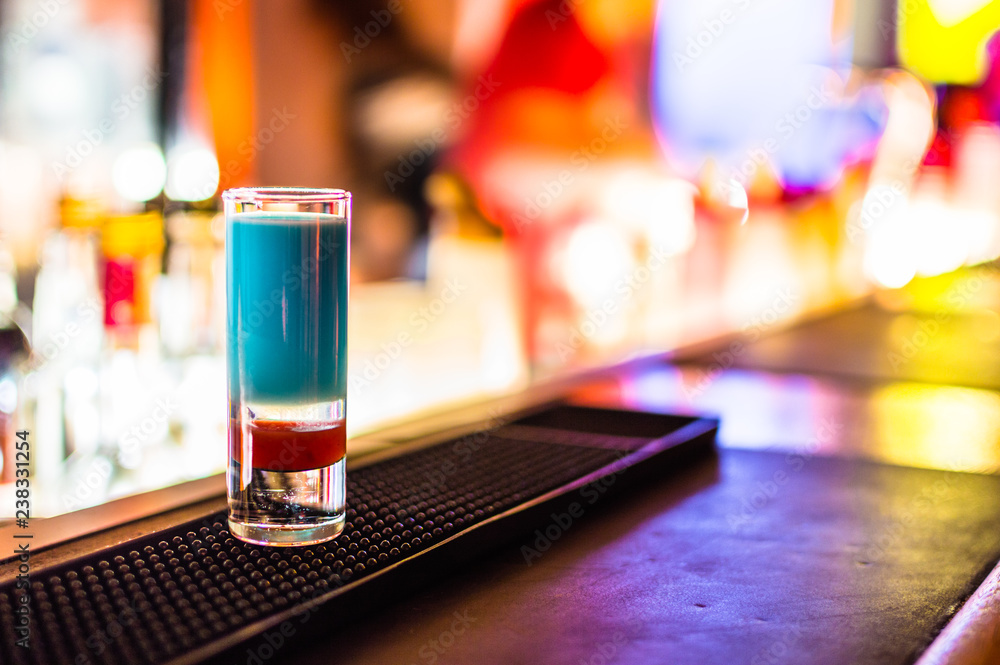 colored and beautiful Chupito drink with bokeh blurred background of an animated and illuminated pub with people moving behind