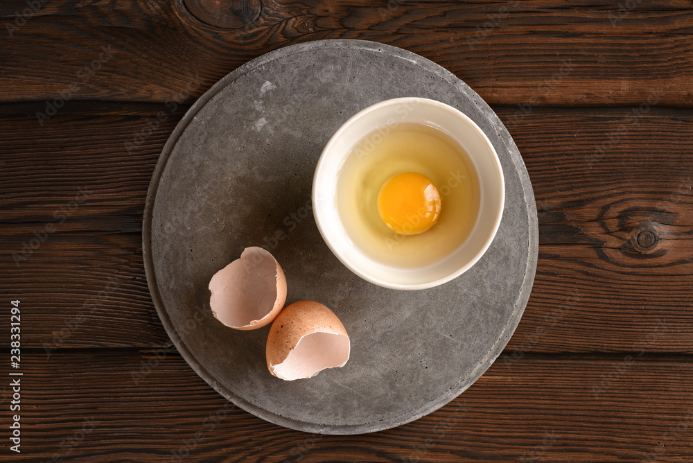 plate with raw broken egg, shell on concrete slab plate with raw broken egg, shell on concrete slab