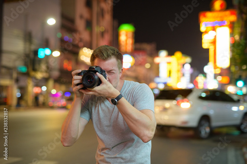 Young tourist man photographing with camera in the streets of Chinatown at night