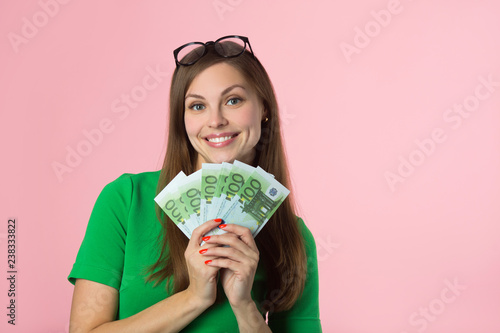 beautiful young girl in glasses holds euro on a pink background photo