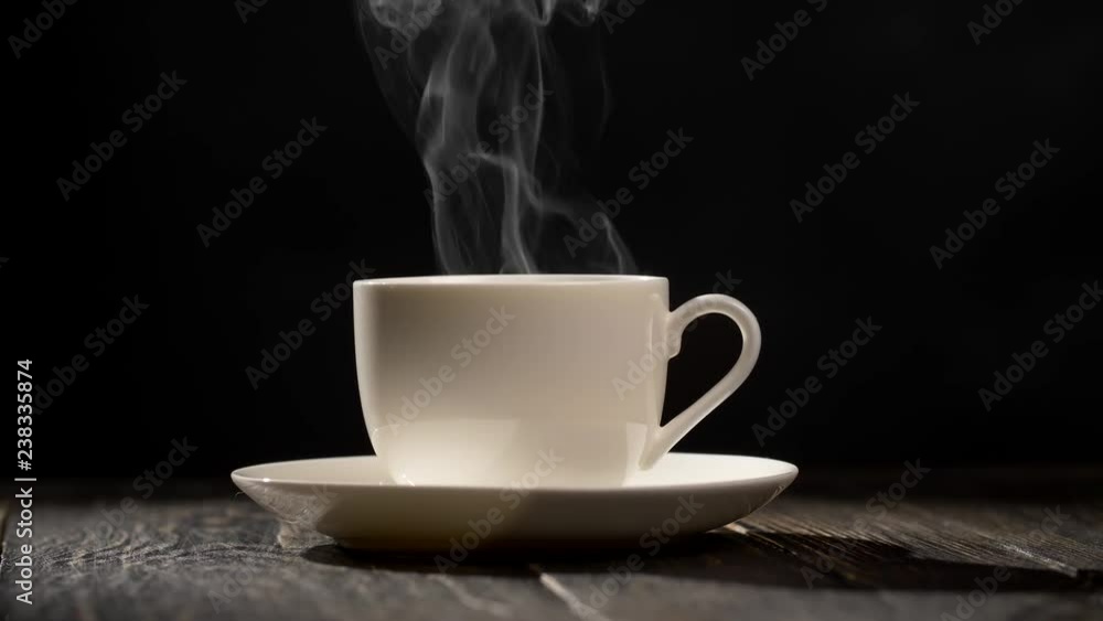 Cup of hot coffee. Steam coming out of a coffee cup standing on a white saucer on a wooden table. Close-up shot with a black background, UHD Cup of hot coffee. Steam coming out of a coffee cup standing on a white saucer on a wooden table. Close-up shot with a black background, UHD