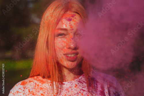 Cool young woman posing in a cloud of pink dry powder, celebrating Holi colors festival