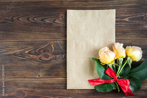 Yellow roses with red bow and greeting card on wooden background. Women's day. Valentines day. Birthday.