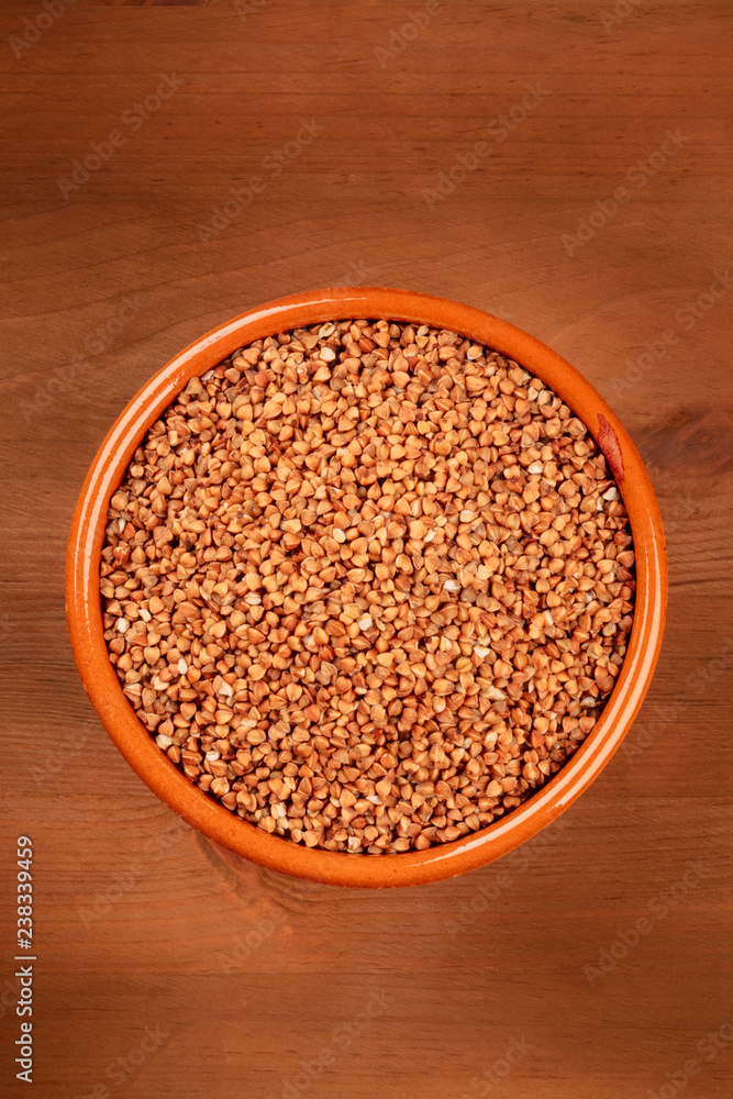 A photo of dry buckwheat in an earthenware bowl, shot from above on a dark rustic wooden background with copy space A photo of dry buckwheat in an earthenware bowl, shot from above on a dark rustic wooden background with copy space