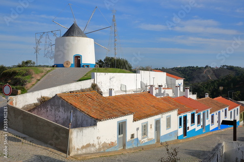 A row of colorful houses along a steep cobbled street inside Odeceixe (near Aljezur), with a whitewashed traditional windmill, Costa Vicentina, Algarve, Portugal