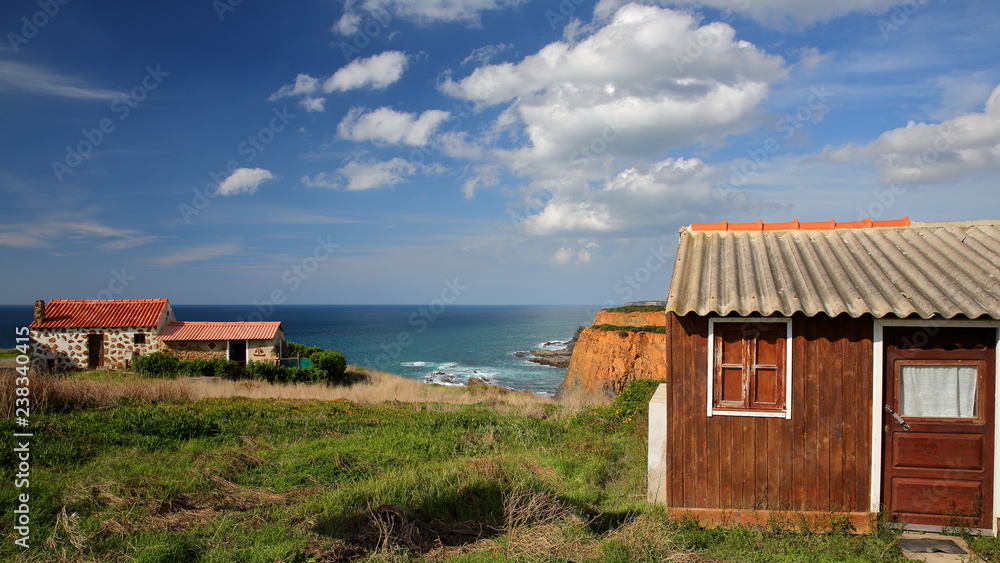 Colorful Fisherman's huts on Alentejo West Coast with dramatic cliffs in the background, Porto das Barcas, Zambujeira do Mar, Alentejo, Portugal Colorful Fisherman's huts on Alentejo West Coast with dramatic cliffs in the background, Porto das Barcas, Zambujeira do Mar, Alentejo, Portugal