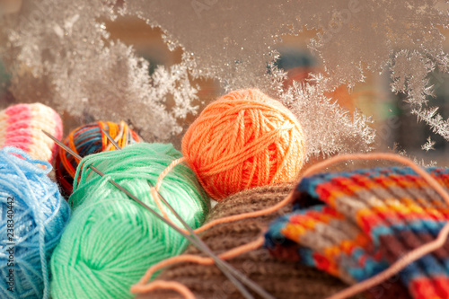 Balls of yarn on the background of a frosty window. Yarn for knitting on a cold winter window-sill on the background of a frosty ice window. Knitting clothes for the cold seasons.