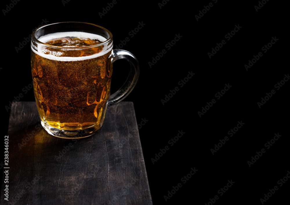 Glass of lager beer with foam and bubbles on vintage wooden board on black background. Space for text Glass of lager beer with foam and bubbles on vintage wooden board on black background. Space for text