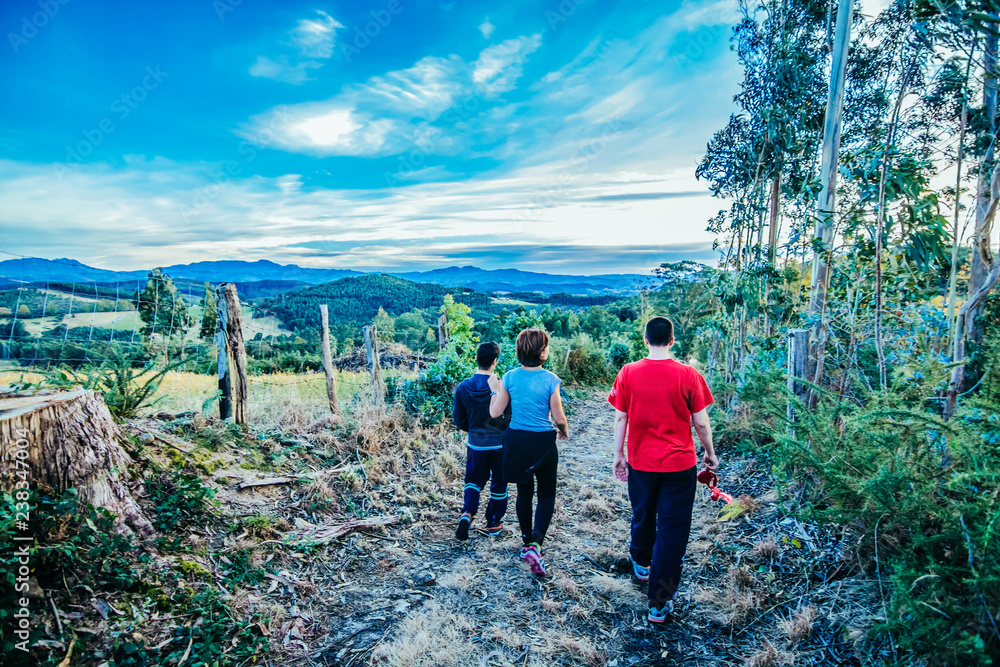 Three young hikers walking on a mountain path under blue and cloudy sky and beautiful landscape on the horizon.