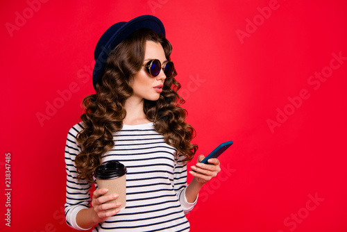 Portrait of nice confident rich wealthy lovely attractive wavy-haired lady wearing striped pullover sunhat holding papercup cacao writing sms isolated over bright vivid shine red background
