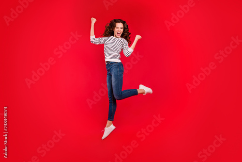 Full length size body portrait of jumping high beautiful pretty charming she her girl raised hands wearing white striped casual sweater and jeans on red vivid bright background