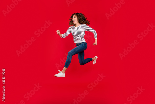 Full length size body photo of fly high charming she her girl quickly running to store shopping mall selling wearing white casual striped sweater denim jeans on red vivid bright background © deagreez