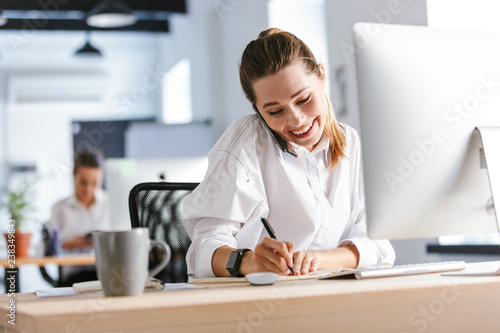 Cheerful young businesswoman sitting at her workplace photo