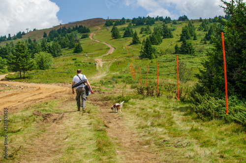 Man hiking with his dog on a path through a hill in summer