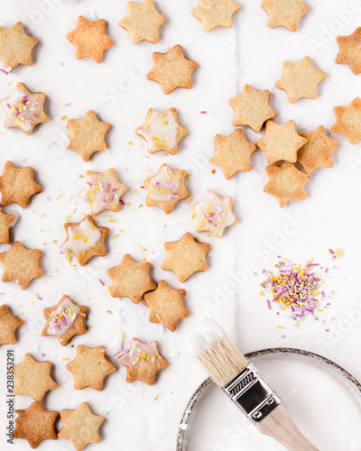 Plätzchen / Kekse gebacken für Weihnachten in Sternform mit Zuckerguss und bunten Streuseln auf weißem Hintergrund von oben bei Tageslicht fotografiert