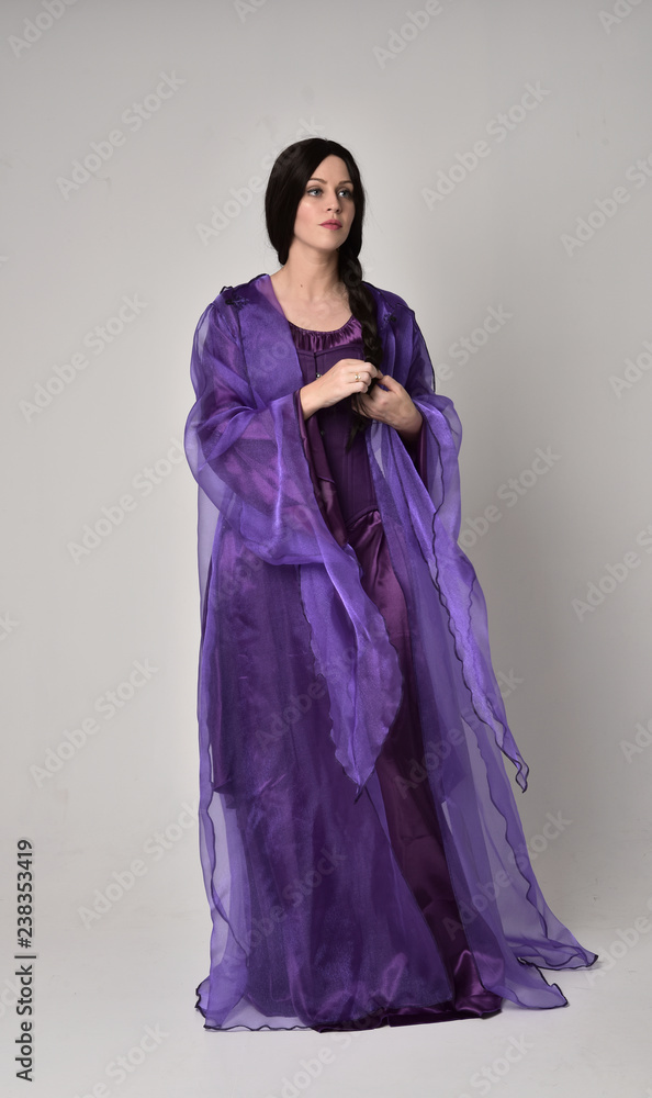 full length portrait of beautiful girl with long black hair, wearing purple fantasy medieval gown and cloak. standing pose on grey studio background. full length portrait of beautiful girl with long black hair, wearing purple fantasy medieval gown and cloak. standing pose on grey studio background.