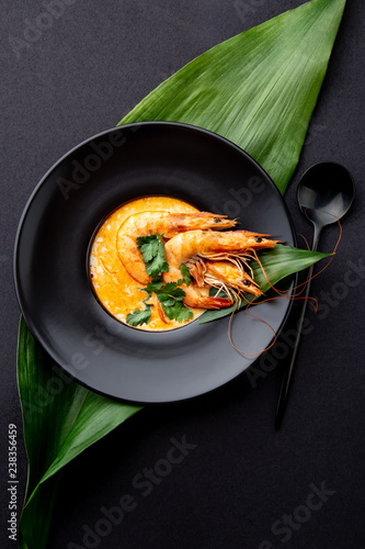 Seafood Soup decorated with whole shrimps and tropical leaves on black plate, black background photo