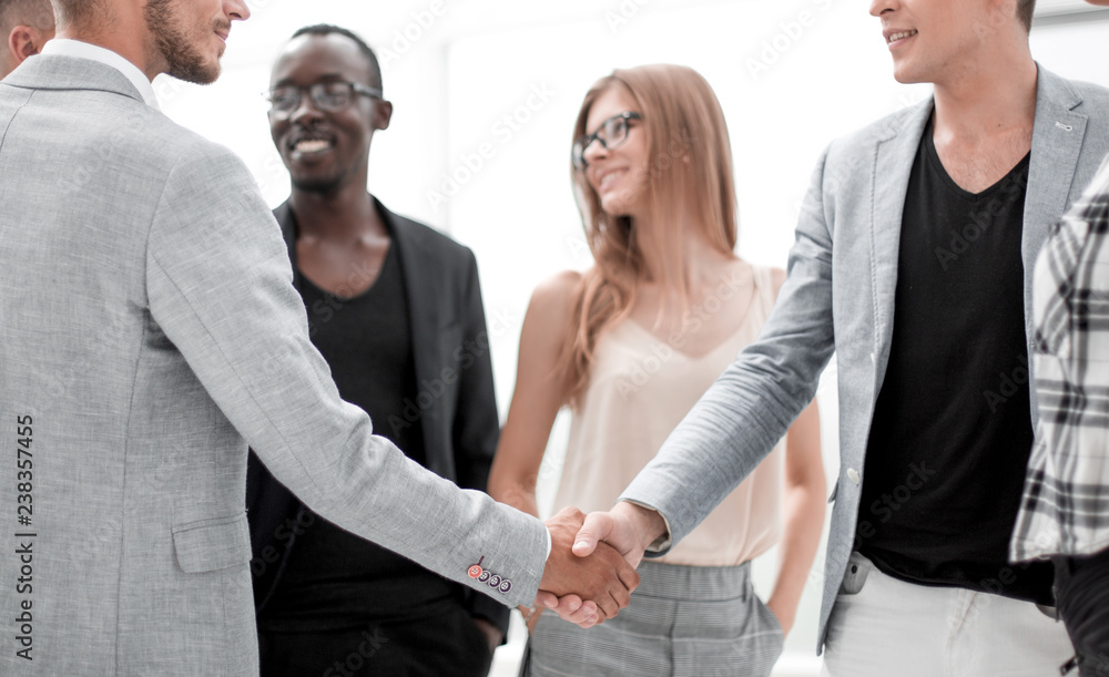 group of young people in the office.two businessmen shake hands group of young people in the office.two businessmen shake hands