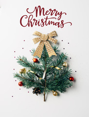 top view of green pine branch decorated as festive christmas tree with bow on white background with "merry christmas" lettering