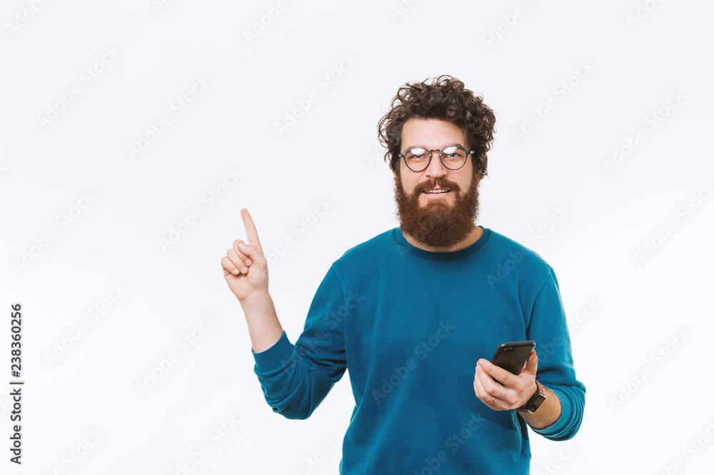 Naklejka premium Portrait of man pointing away at copyspace and holding smartphone