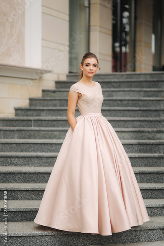 Elegant brunette stand on stairs by the hotel. Fashion model in evening dress