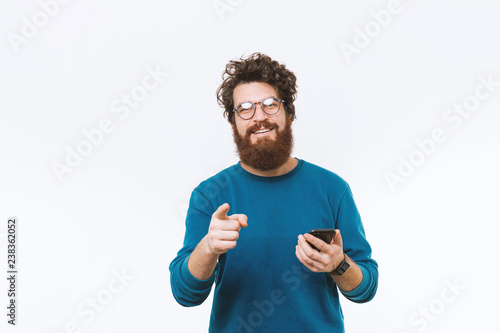 Happy smiling bearded man pointing at the camera and holding smartphone