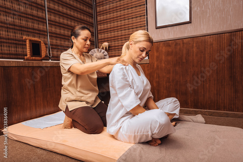 Professional female masseuse massaging her clients shoulders