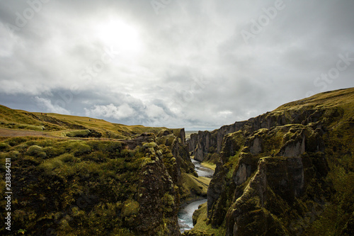 Fototapeta Naklejka Na Ścianę i Meble -  Deep canyon, steep cliffs overgrown with green moss, surrounded by a very fast river with cold water. Canyon of Icelandic tales - Fjardrarglufur