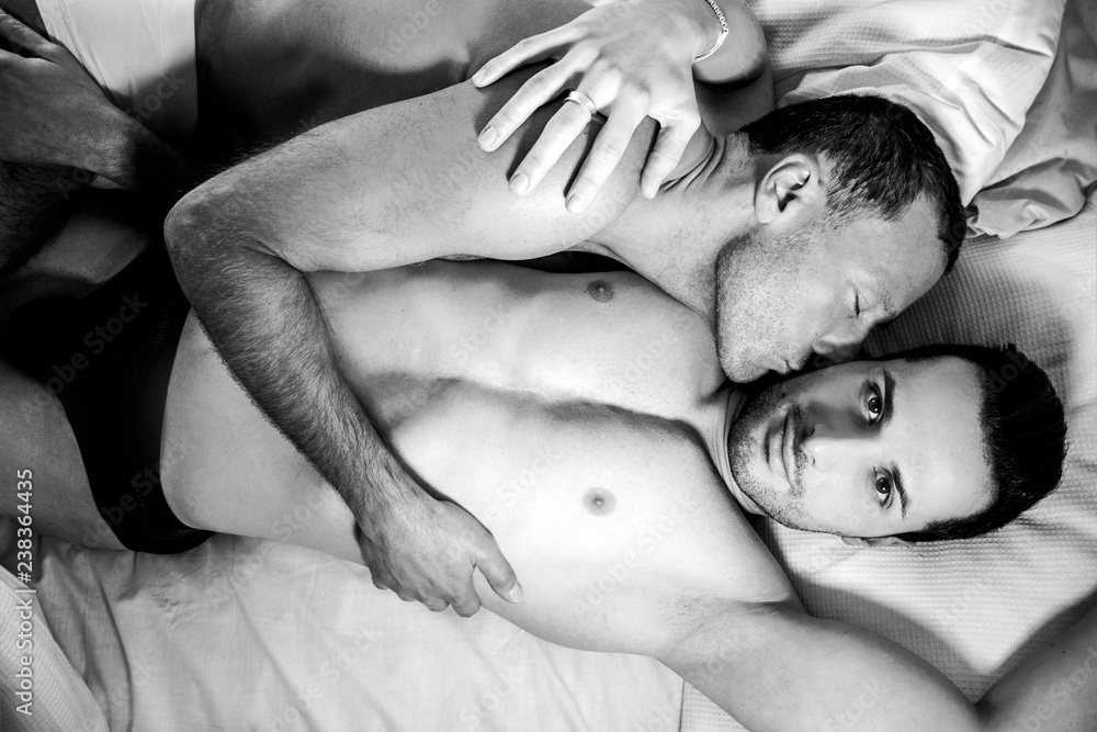 Attractive male gay couple lying together in bed, one kissing other looking  at camera foto de Stock | Adobe Stock