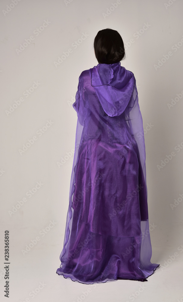 full length portrait of beautiful girl with long black hair, wearing purple fantasy medieval gown and cloak. standing pose on grey studio background. full length portrait of beautiful girl with long black hair, wearing purple fantasy medieval gown and cloak. standing pose on grey studio background.
