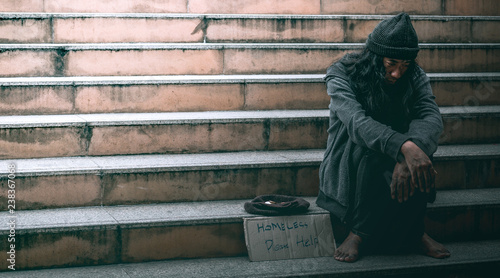 Poor homeless man or refugee sitting on the stairs at urban street in the city begging for money.