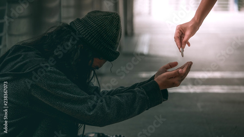 Poor homeless man or refugee sitting on on the dirty floor recieving money.