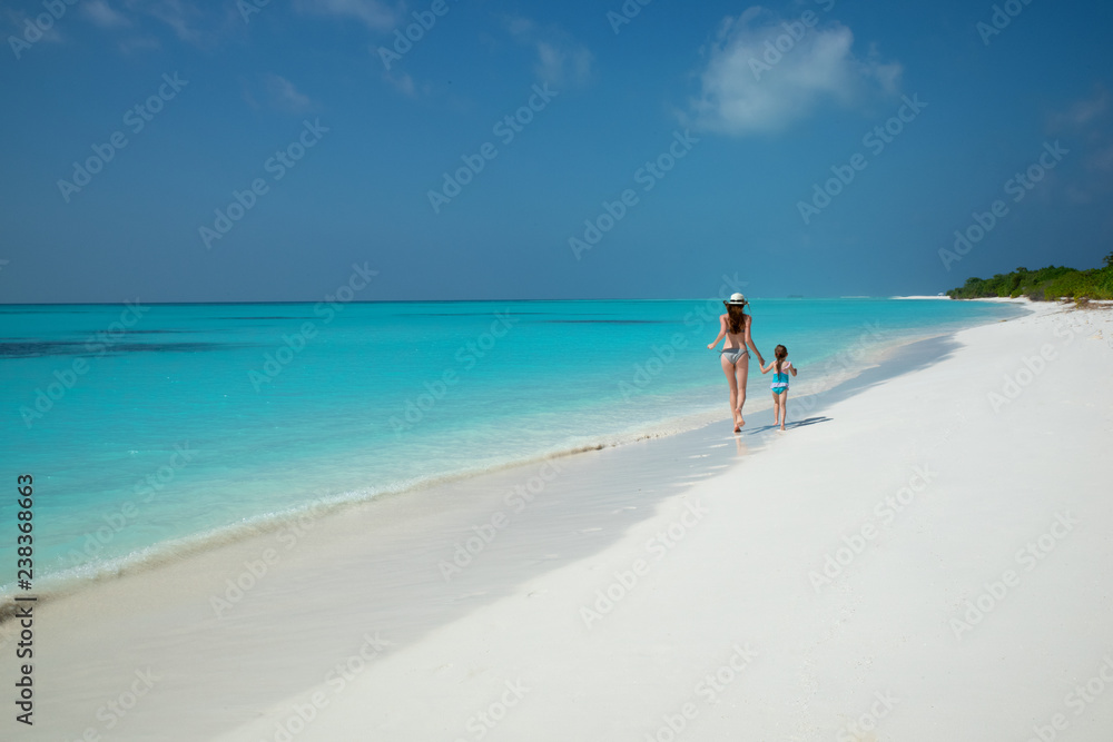 Happy mother and daughter running on Maldives beach on sunny day