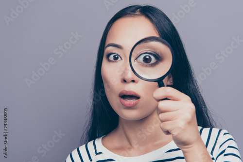 Close-up portrait of nice attractive scared speechless straight-haired lady in striped pullover holding looking through loupe opened mouth omg isolated on gray pastel background