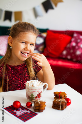 Wallpaper Mural Little girl in red dress eating Christmas cookies with cacao in cup, red Chirstmas decorations around Torontodigital.ca