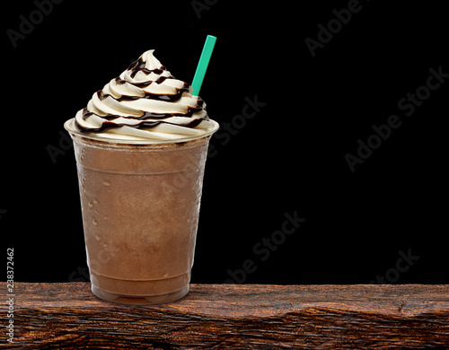 Fotografie Iced coffee or frappuccino with cream in take away disposable cup mock up or mockup template isolated on wooden table with black background