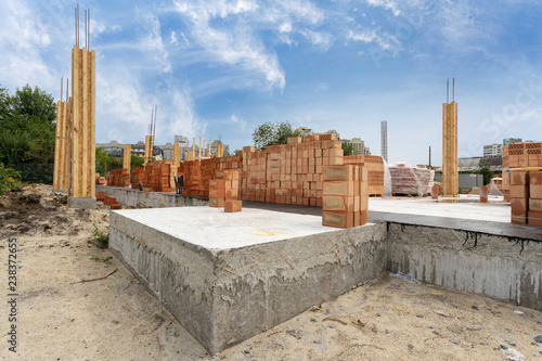 Side view of house support elements and new brick wall. Beginning of the construction residential building with wooden and concrete column formwork against blue sky