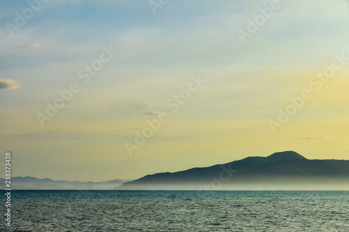 beautiful line of sea and blue-yellow sky. majestic mountains in the fog