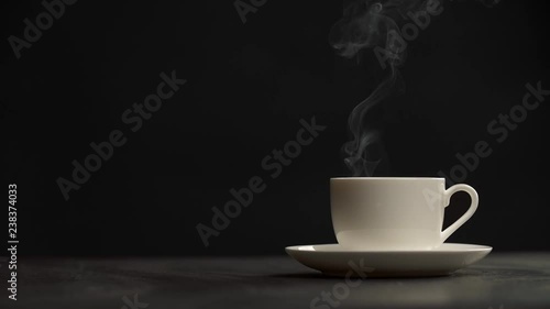 Steaming coffee cup on black background. Puffs of steam slowly coming from a white cup of hottest coffee. Slow motion shot