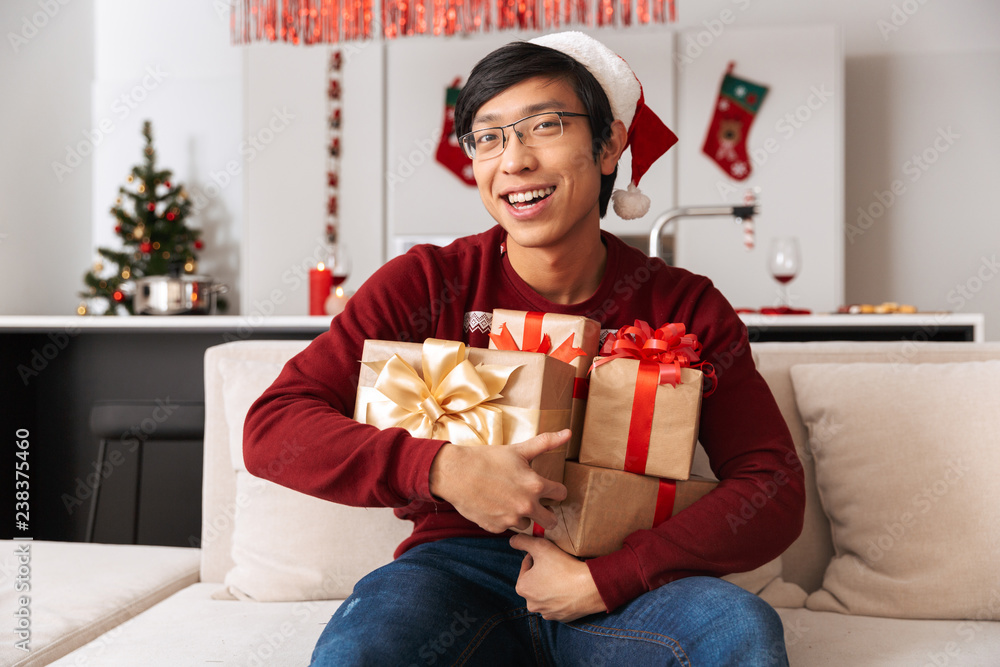 Portrait of cheerful man sitting on couch in living room with present boxes, while celebrating New Year Portrait of cheerful man sitting on couch in living room with present boxes, while celebrating New Year