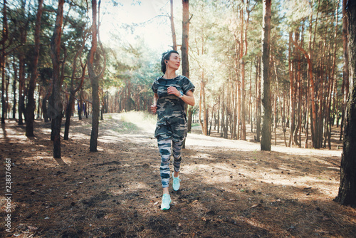 Young fitness woman running at morning. Woman wearing military-colored clothing and smart watch